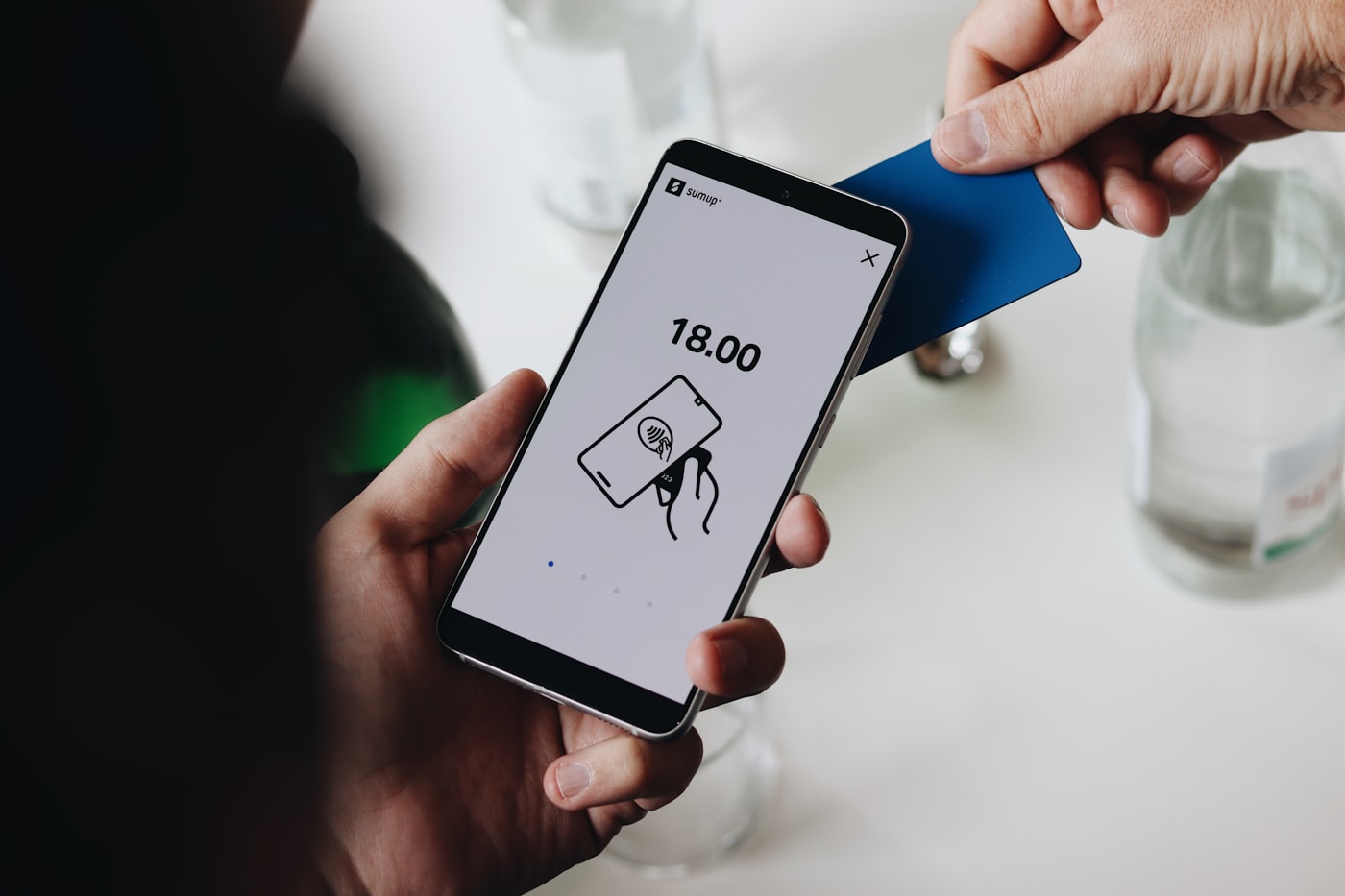 A buyer tapping a card against a phone showing a checkout total